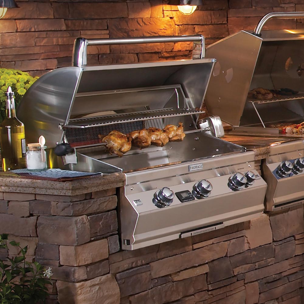 Rotisserie grill setup with stainless hood, spit rod, and rotating chicken over grates