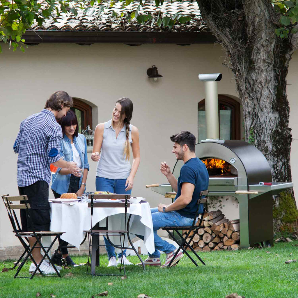 Wood-fired countertop pizza oven in outdoor party setup with flames inside