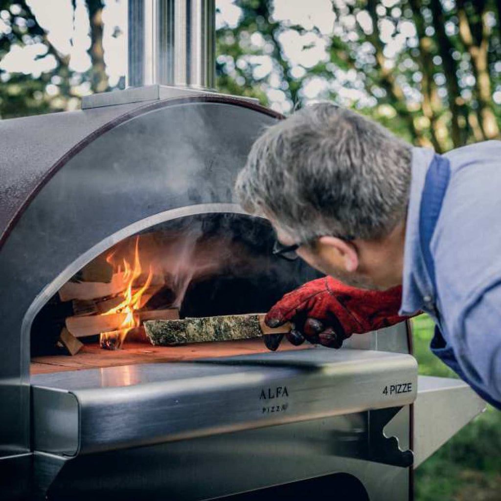 Wood-fired pizza oven opening with fire, logs, and a pizza-loading tool