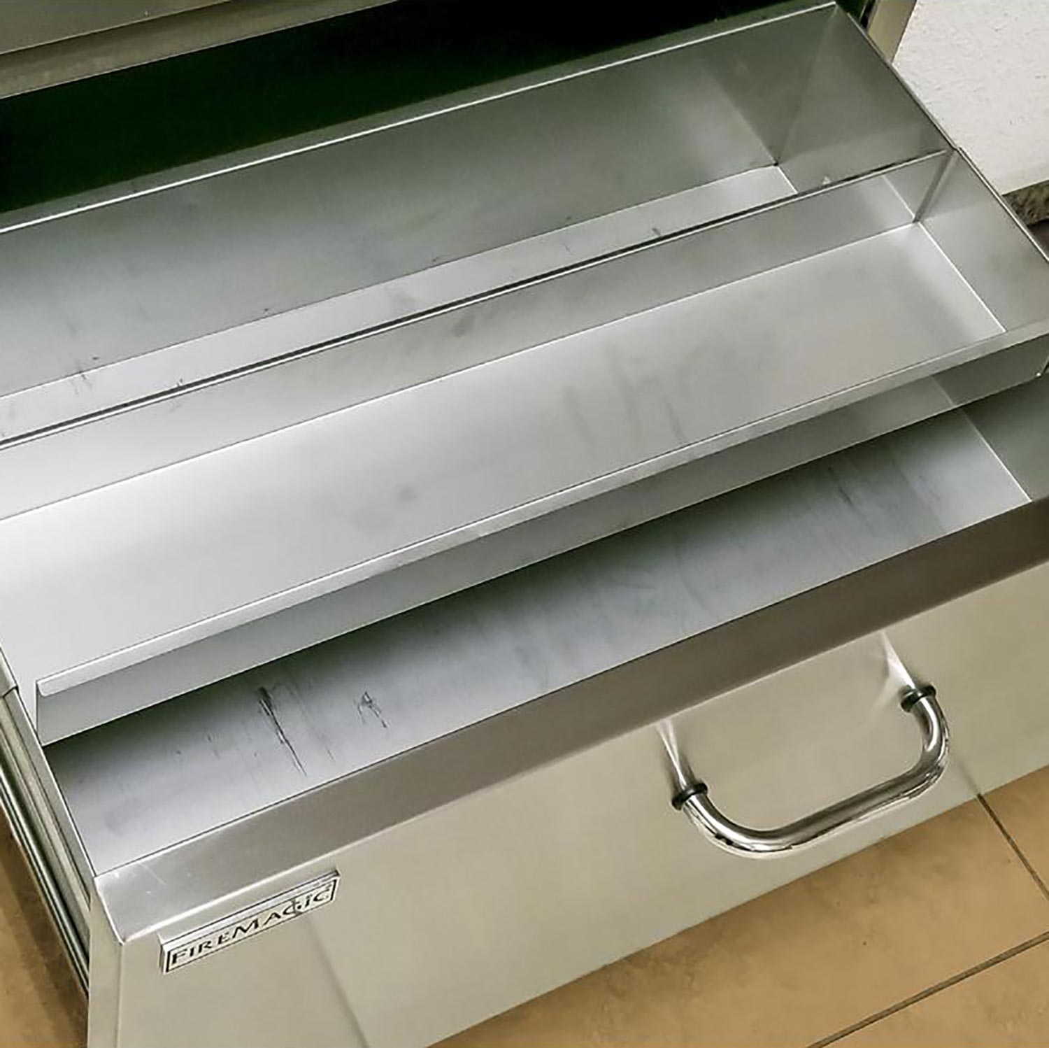 Open flush masonry drawer showing stainless interior with Fire Magic logo and handle.