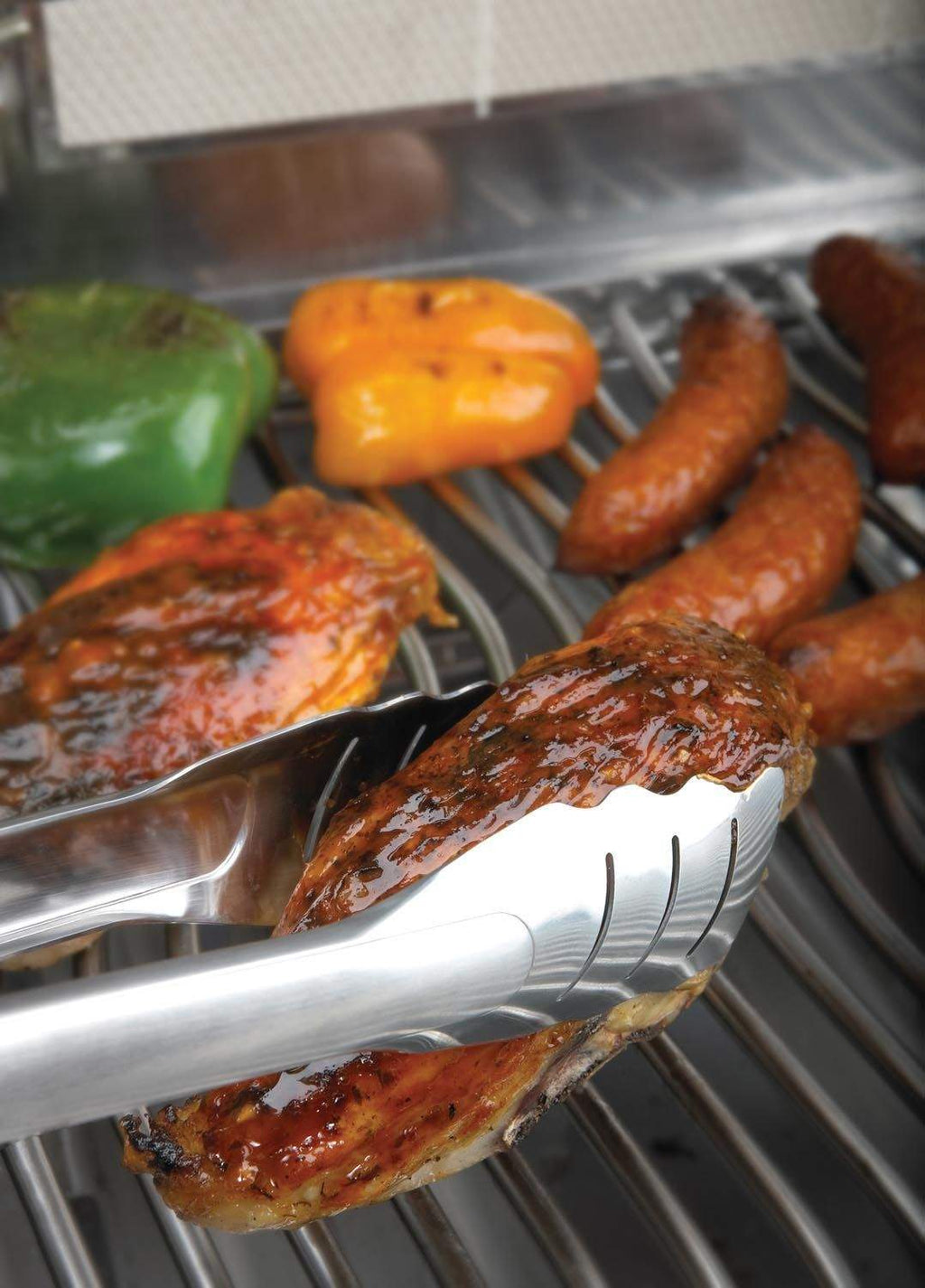 Stainless steel locking tongs gripping grilled sausages on a barbecue grate