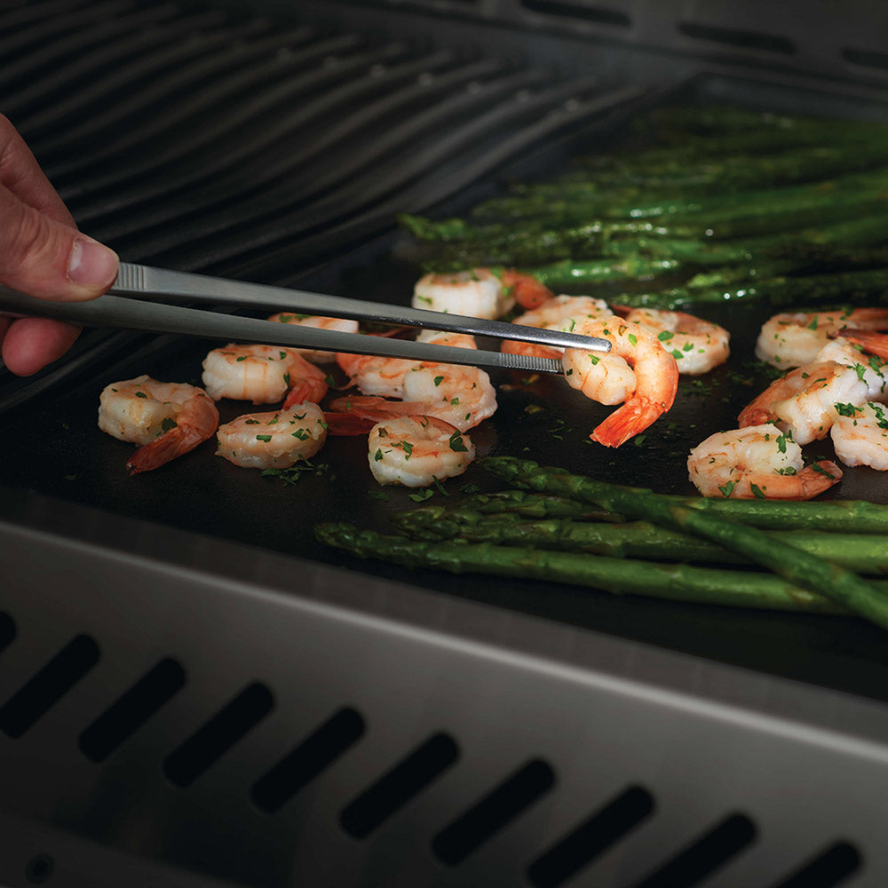 Stainless steel grilling pincer tongs gripping shrimp on a grill