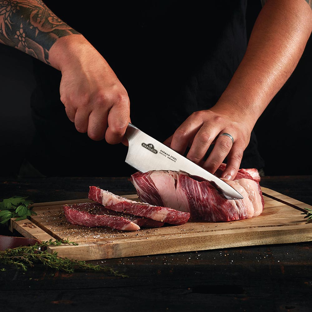 Napoleon chef's knife slicing meat on a wooden cutting board