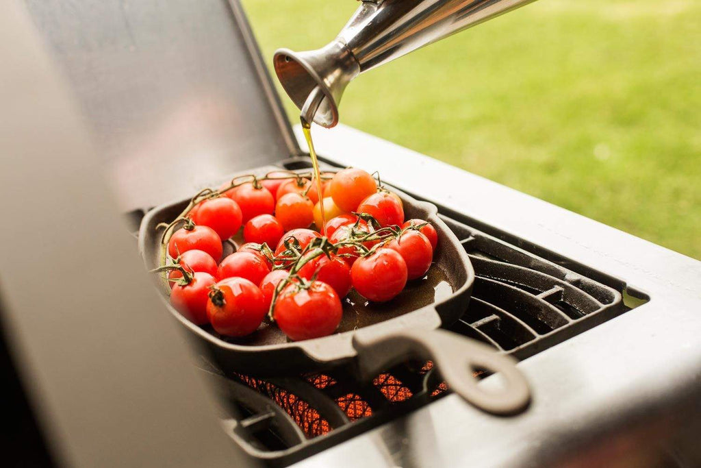 Cast iron sizzle platter skillet with cherry tomatoes, oil pouring while on grill
