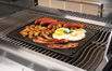 Dark cast iron reversible griddle on grill, showing browned food on surface