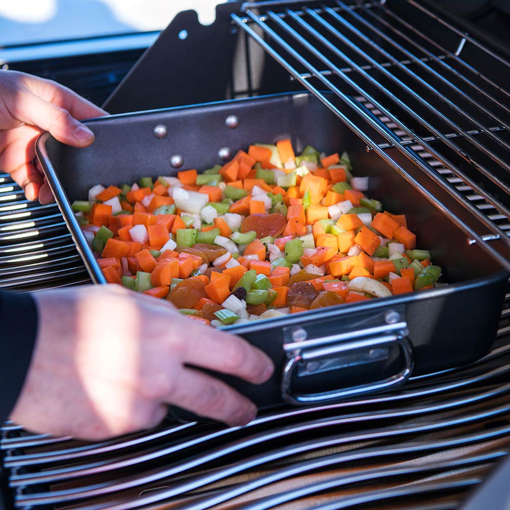 Black roasting pan with handles, holding diced vegetables on grill rack