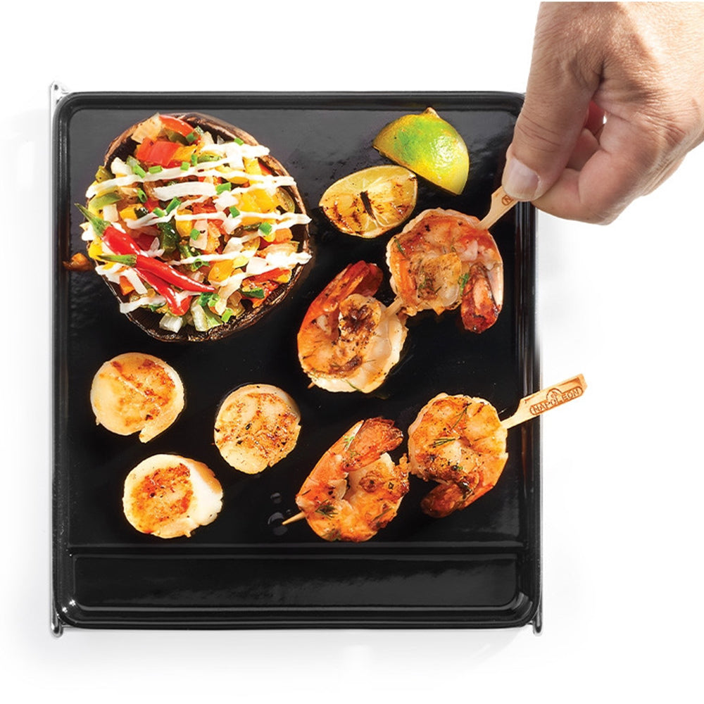 Cast iron griddle with grilled shrimp, chicken pieces, and sliced vegetables, black surface