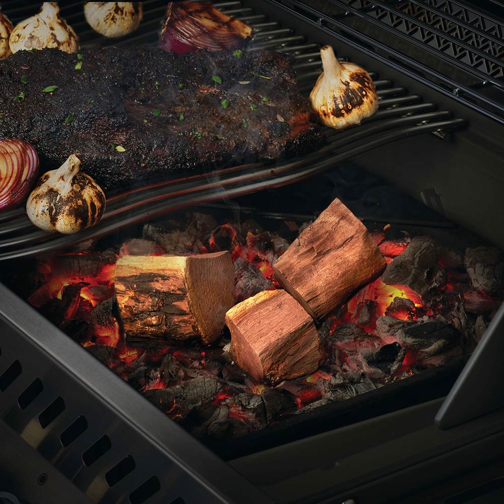 Mesquite wood chunks on grill grate over red embers