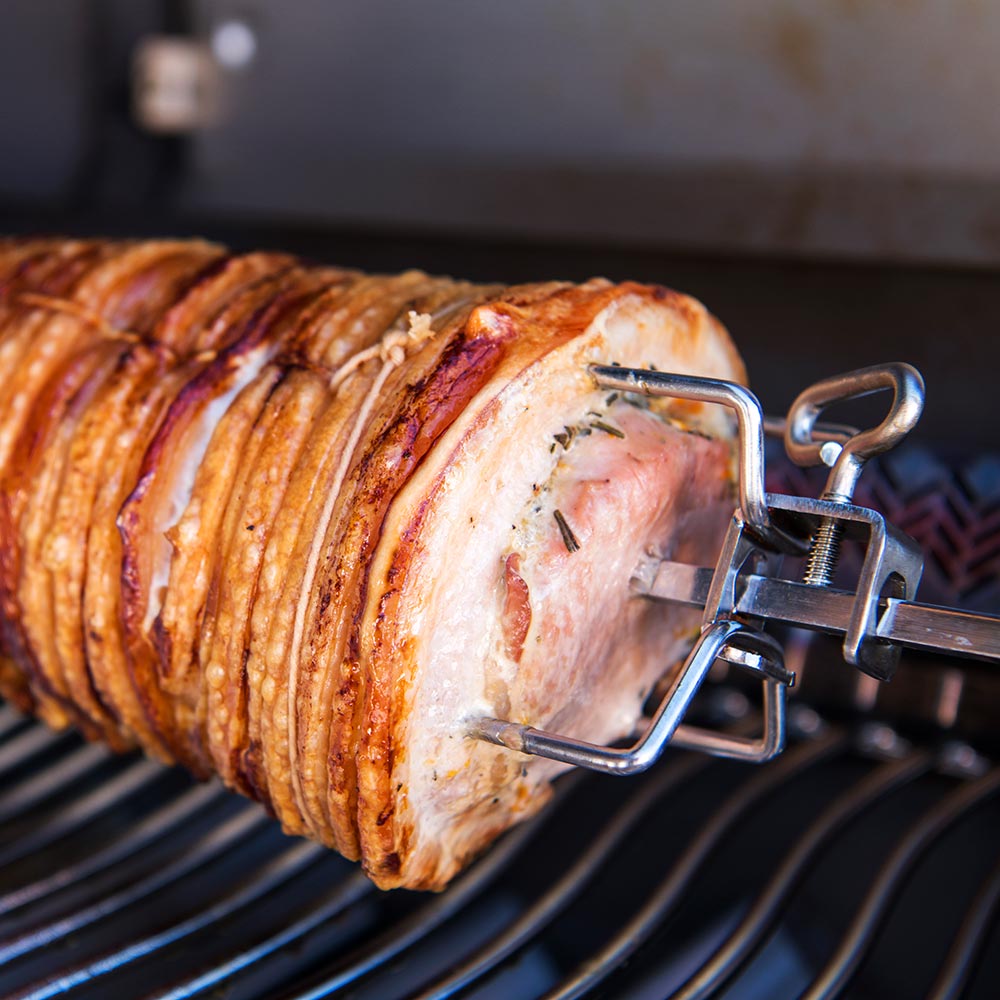 Rotisserie-cooked meat on a spit rod with metal clamps