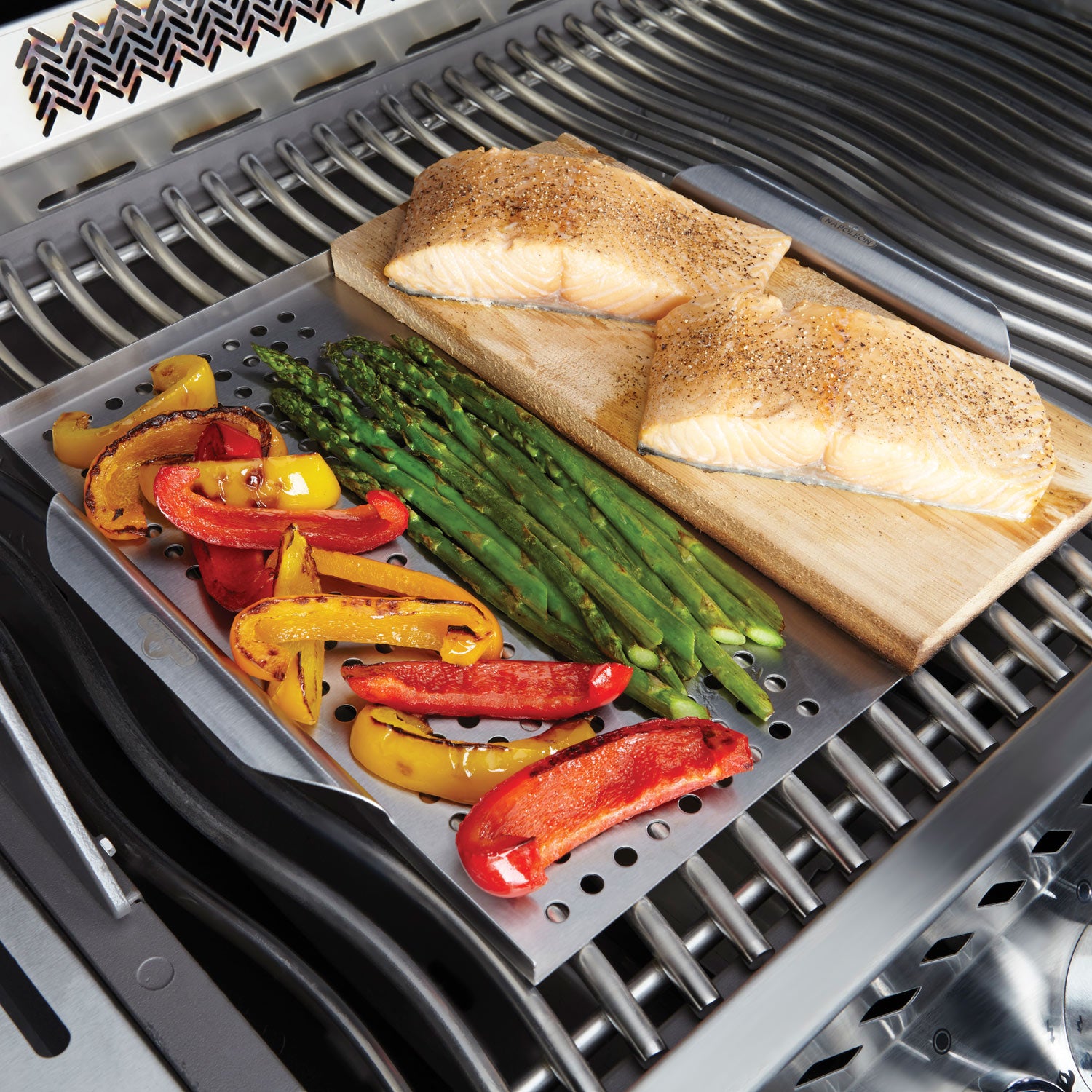 Stainless steel topper with cedar plank on grill grate, with vegetables and fish