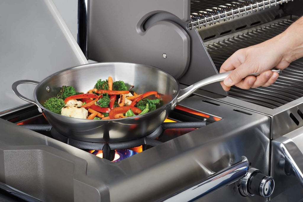 Stainless steel wok on gas grill with cooked vegetables and shrimp