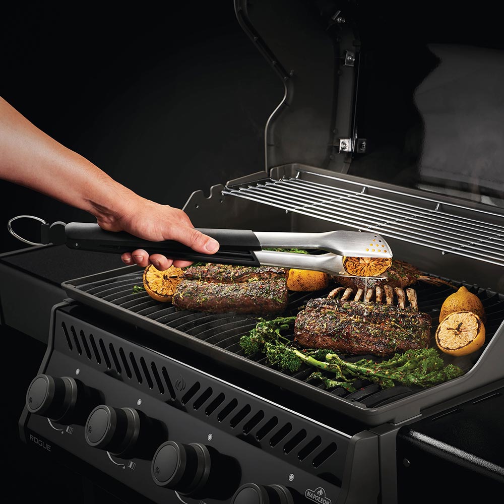 Stainless grilling spatula with black handle, lifting food on grill