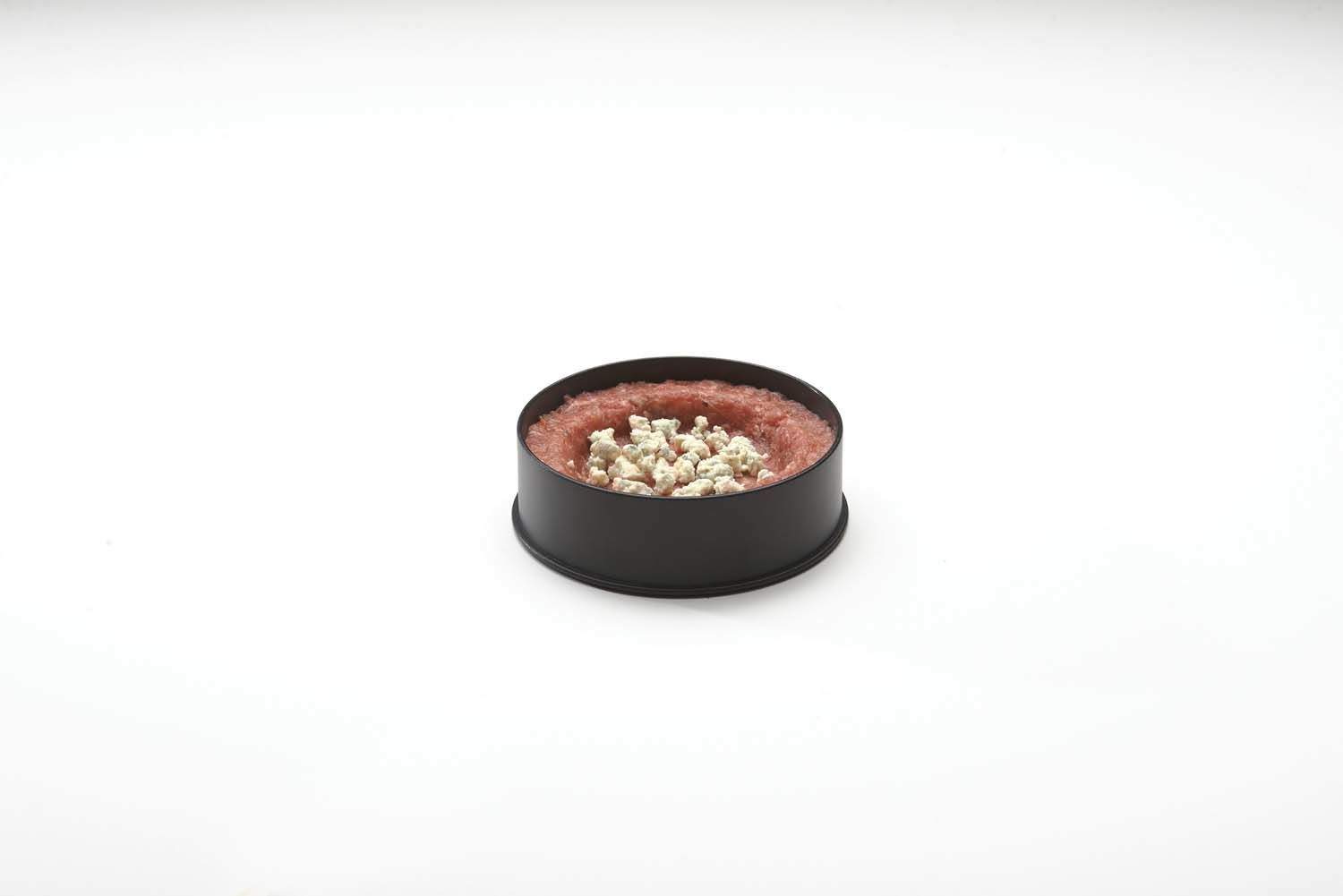 Burger patty mixture in black round mold, with pale pieces visible