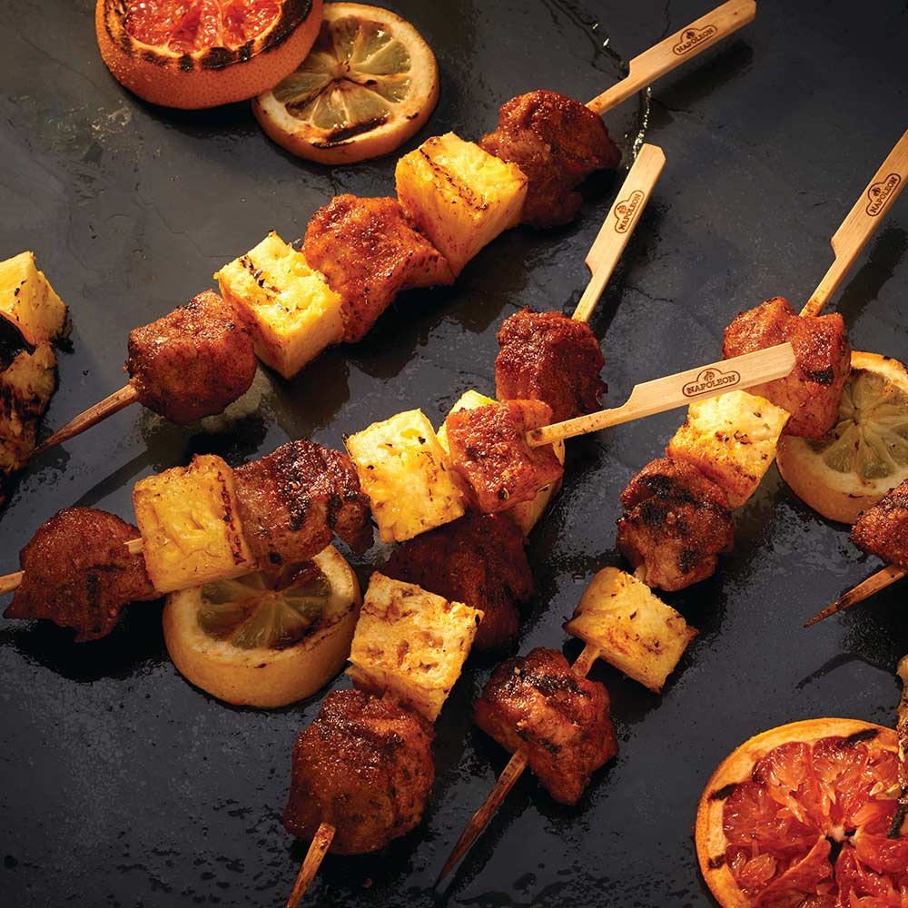 Bamboo skewers with meat and onion pieces on dark grill