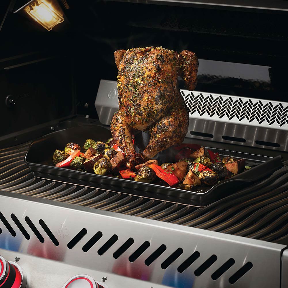 Roasting pan holding a beer-can chicken over vegetables on a grill rack