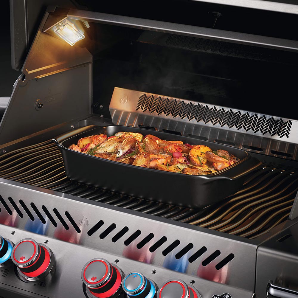 Black ceramic casserole dish on grill grate with lid off, filled with roasted food