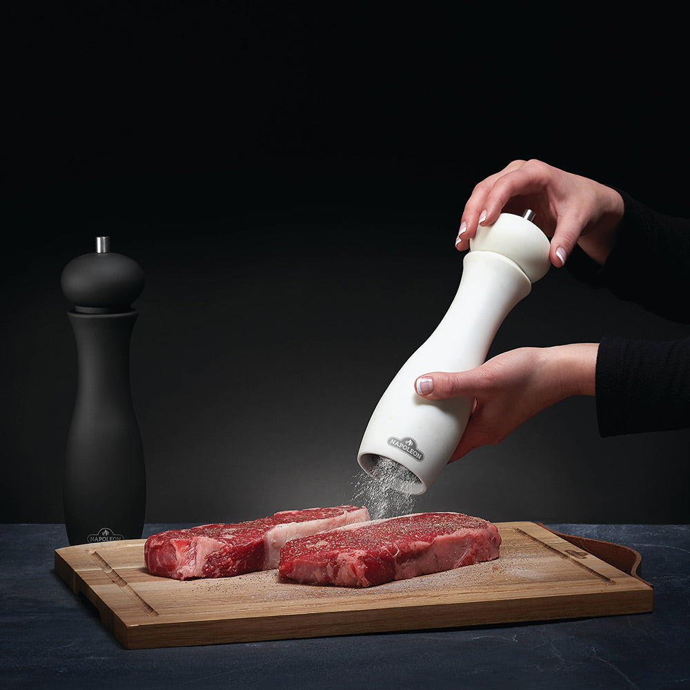 White salt grinder in use with hand over meat on cutting board