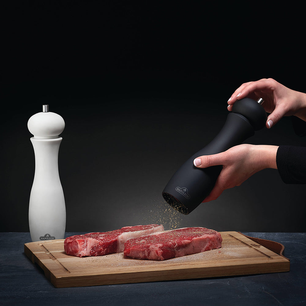 Black pepper grinder in hand, grinding over meat on cutting board