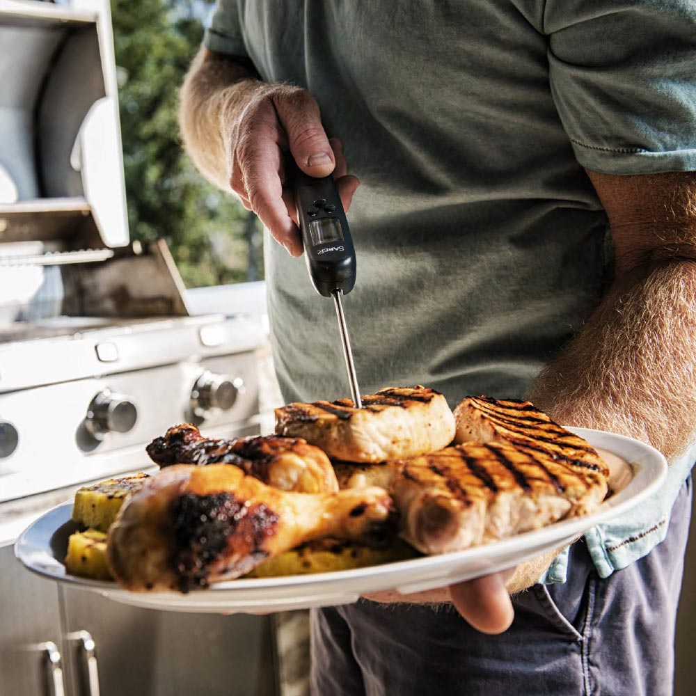 Digital thermometer held over grilled meat on a plate