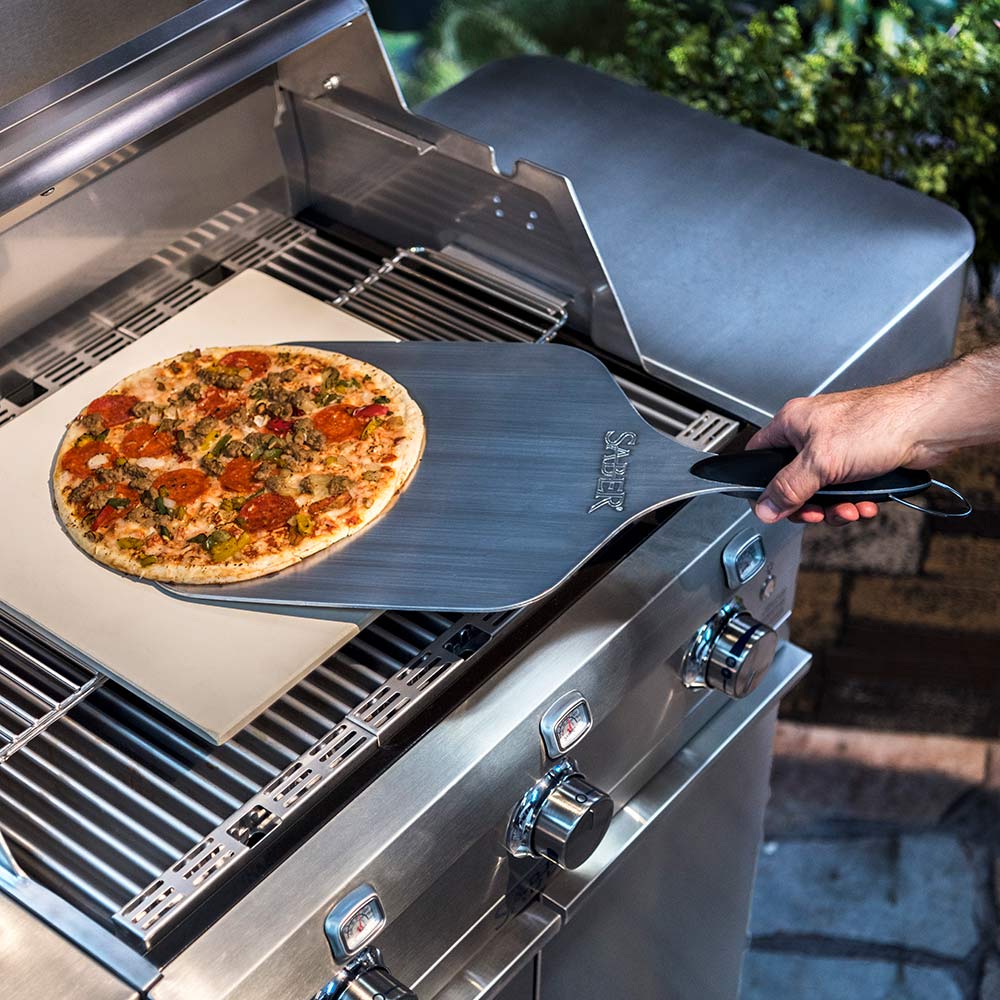 Aluminum pizza peel lifting pizza off a grill rack