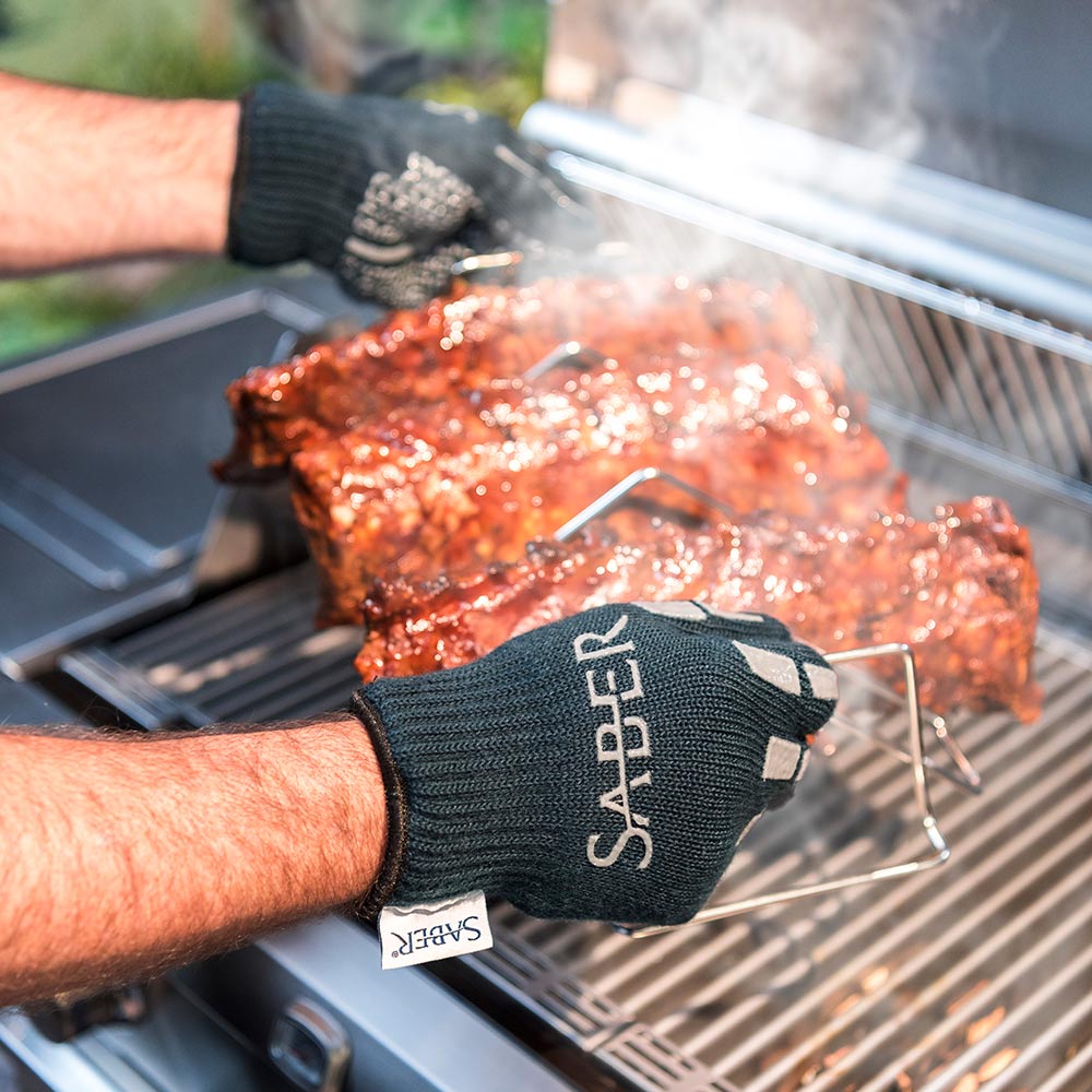 Hand wearing dark navy grill glove with Saber logo, gripping hot roasted meat