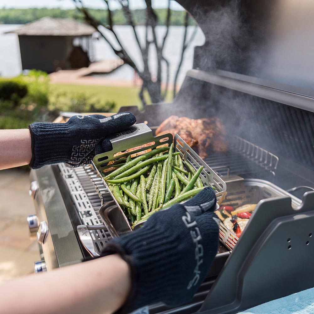Two hands wearing dark navy grill gloves while handling vegetables on grill