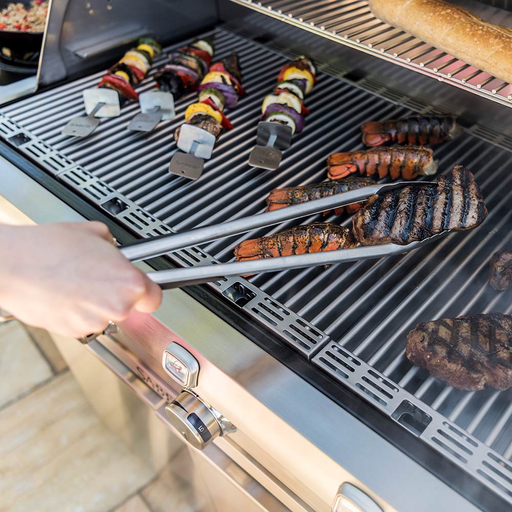 Stainless steel barbecue tongs with loop handle and scalloped ends on grill