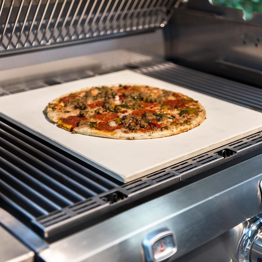 Pizza on square pizza stone on grill, light beige surface