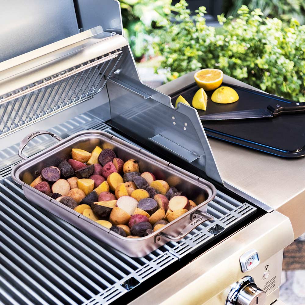 Stainless roasting pan on grill filled with mixed vegetables and lemon slices