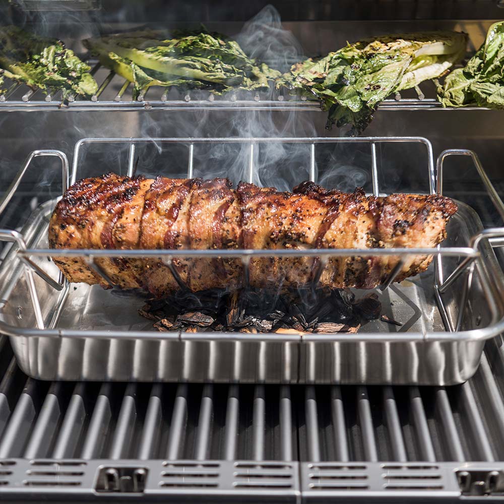 Grill roasting pan holding a whole herb-rubbed meat with smoke