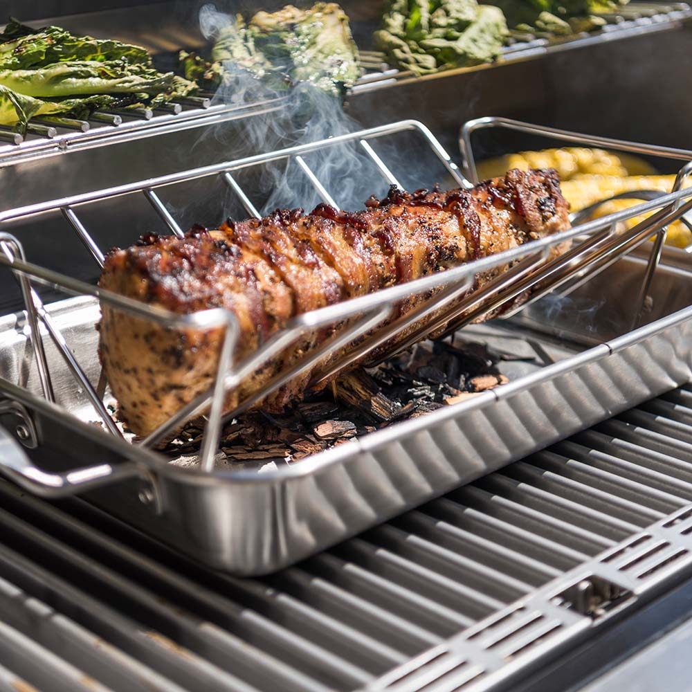Roasting pan on grill with sliced meat pieces and smoke rising