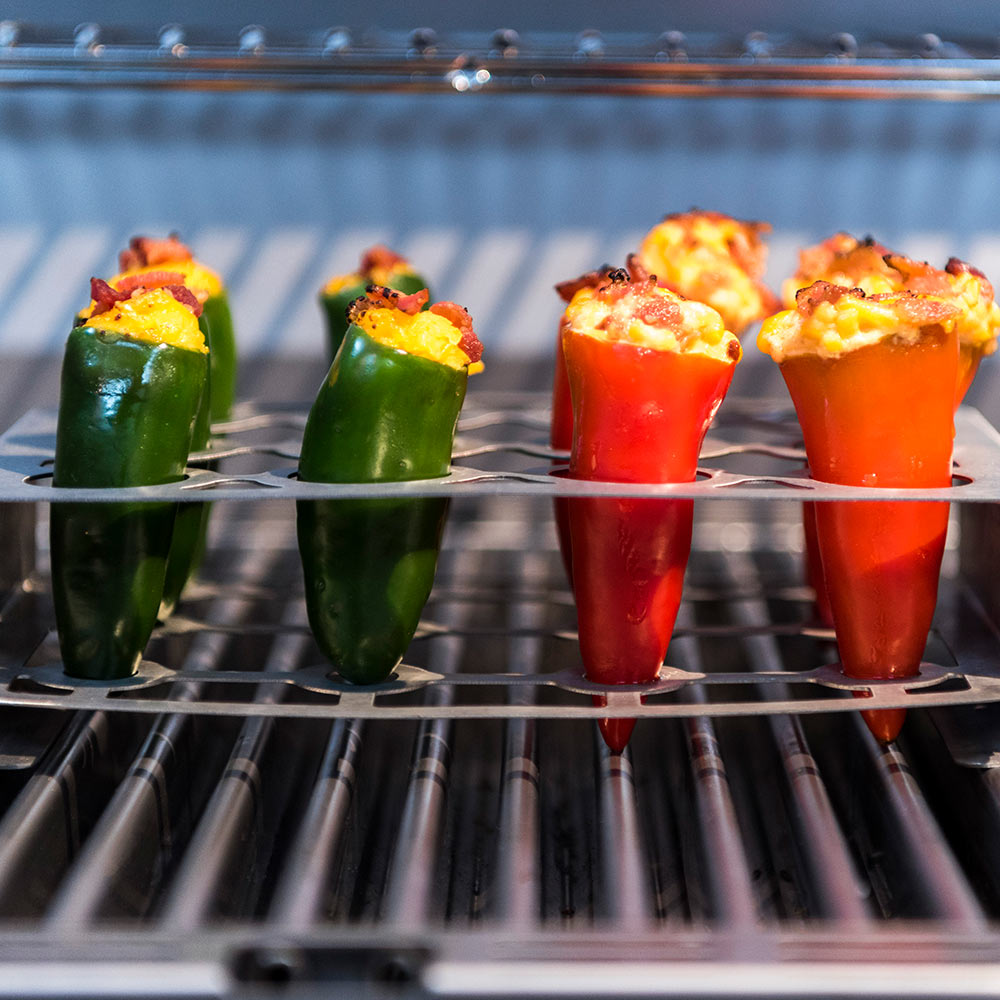 Stainless steel roaster rack holding green and red stuffed peppers on grill