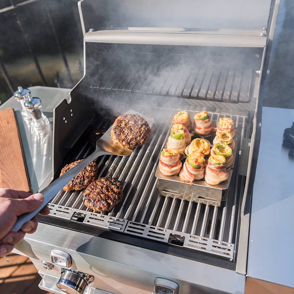 Double pepper roaster tray on grill with stuffed bites and a hand adjusting