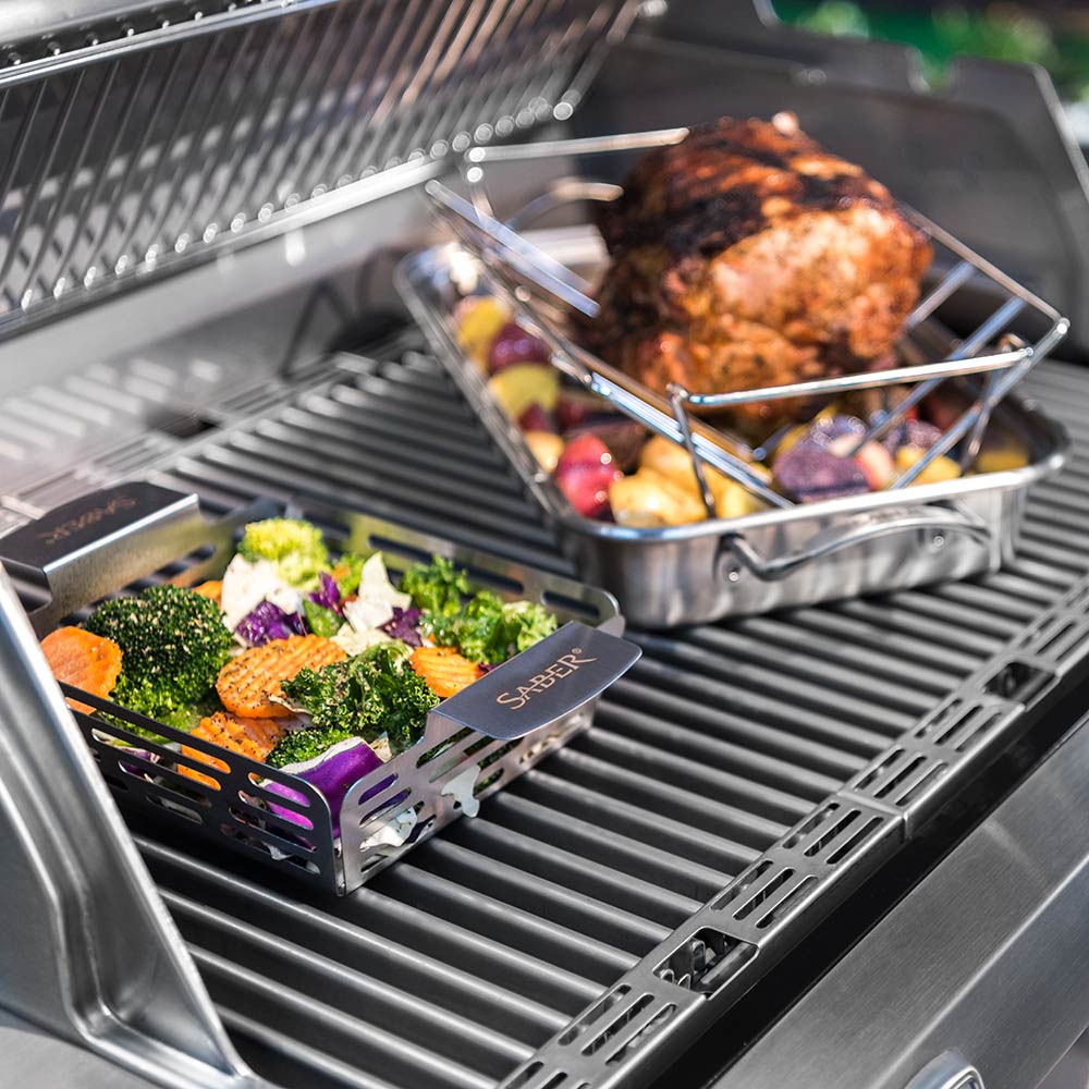 Stainless steel veggie basket filled with vegetables on grill grates, Saber logo