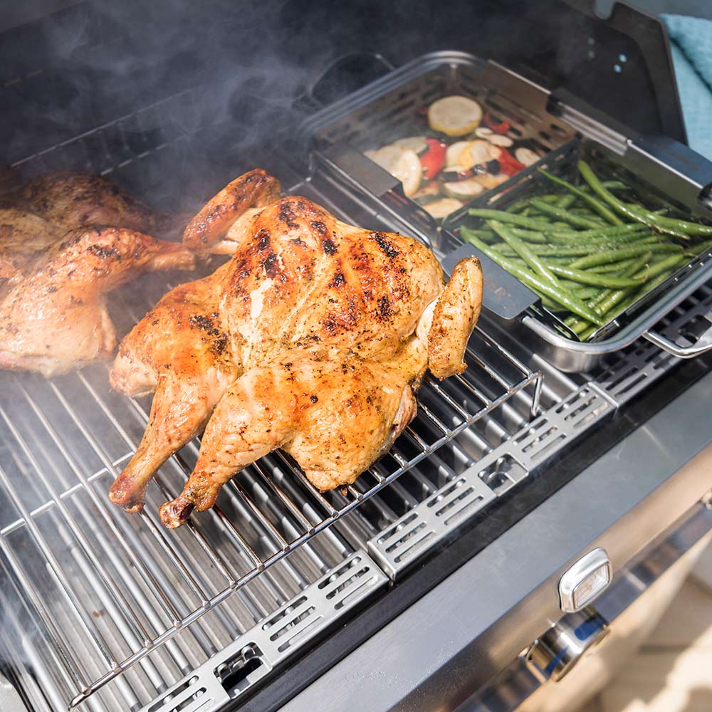 Stainless steel grilling baskets on a barbecue grill with vegetables and smoke