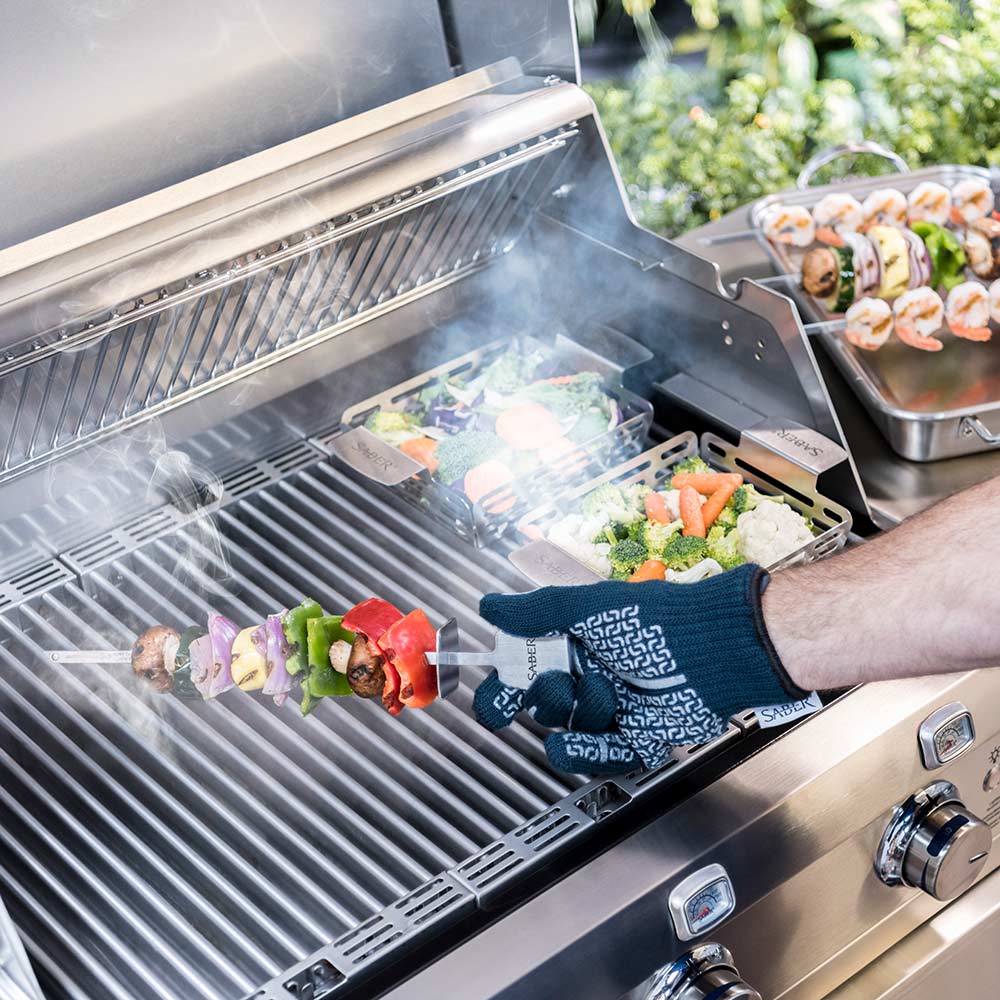 Outdoor grill with wire basket trays and a gloved hand