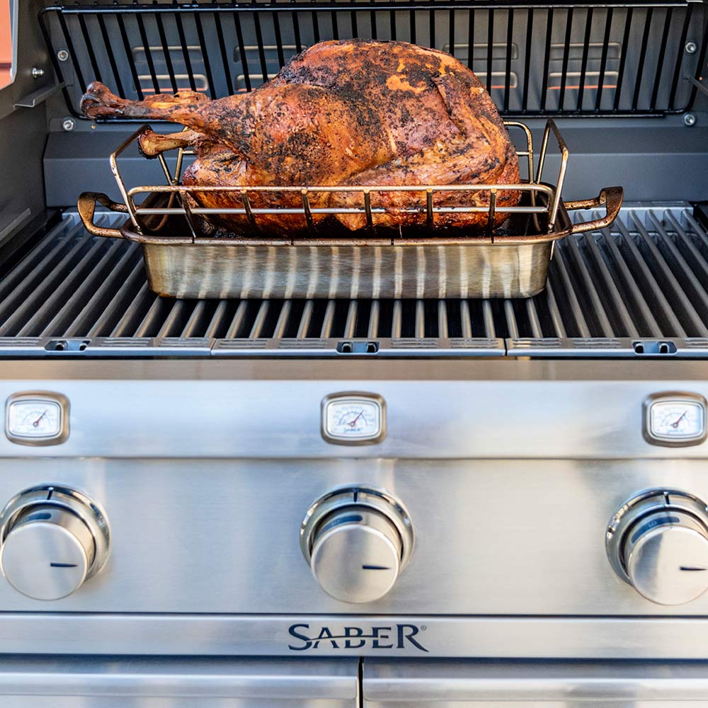Roasting rack holding whole roasted turkey on grill grate, stainless steel
