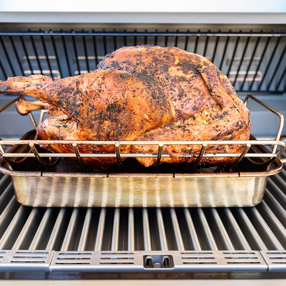 Roasting rack with roasted turkey centered on grill grate, stainless steel wire frame