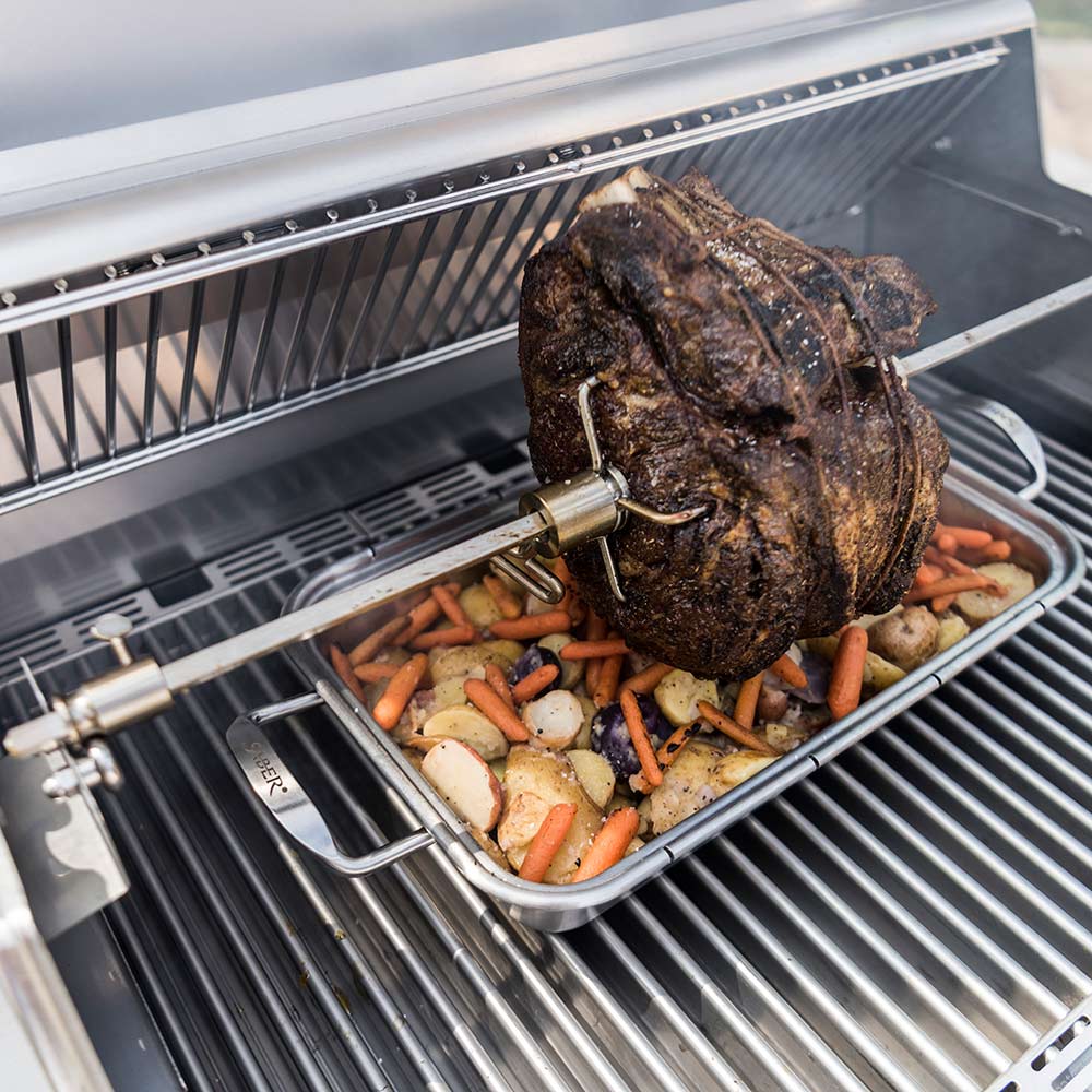 Rotisserie chicken on spit rod roasting on grill grates, with a vegetable tray
