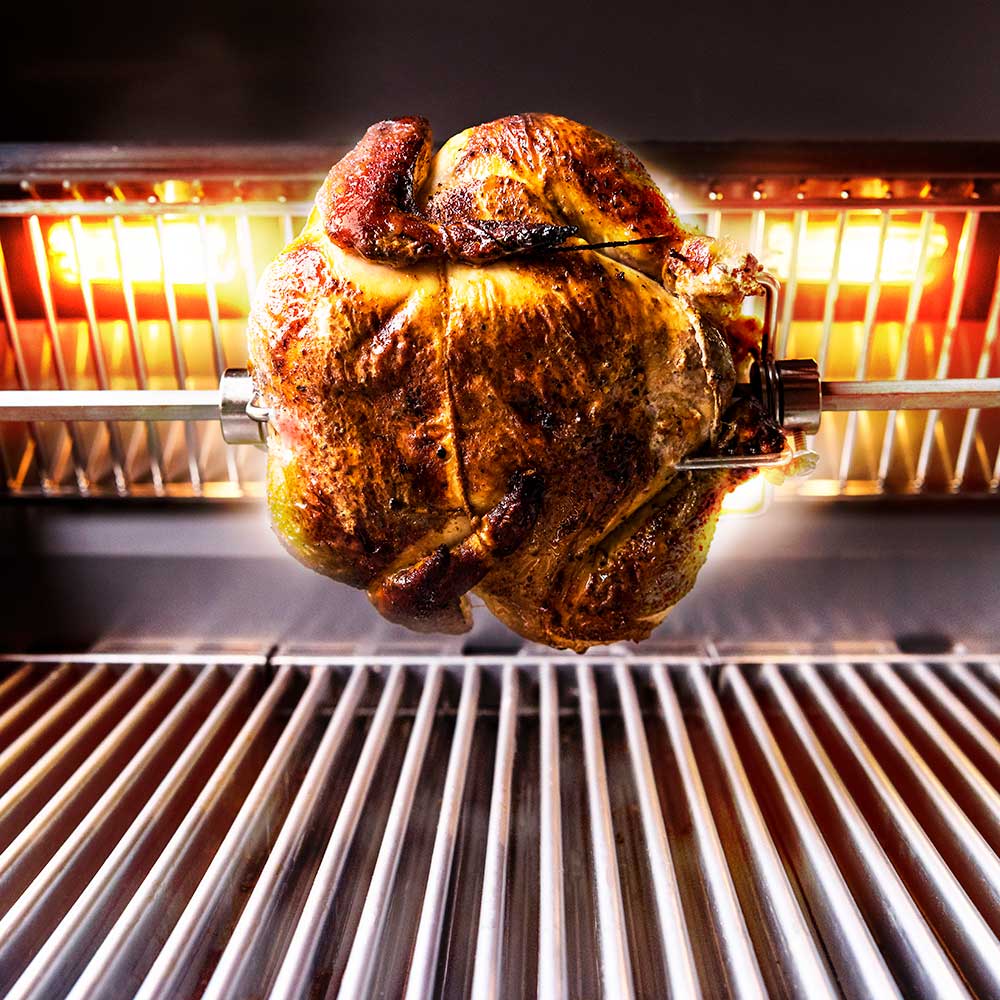 Rotisserie chicken turning on spit rod above glowing grill burners