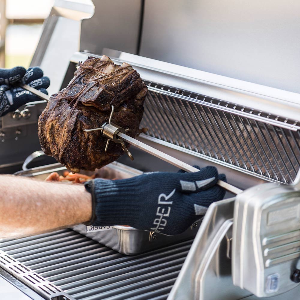 Gloved hands loading rotisserie chicken onto spit rod on a grill
