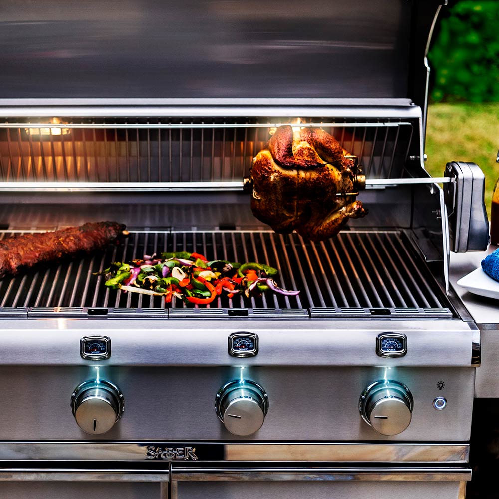 Rotisserie chicken turning on a stainless steel grill with vegetable kebabs