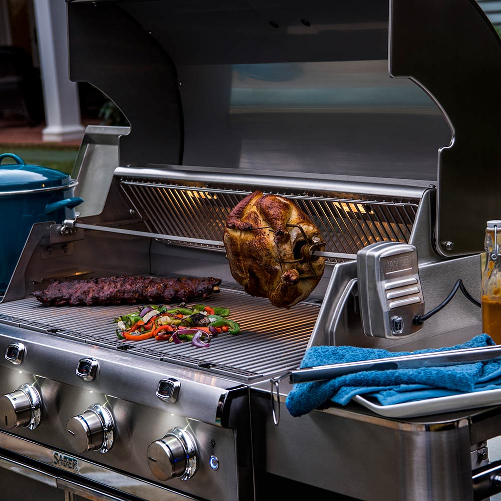 Rotisserie grill with whole chicken and meat on wire rack, stainless side tray