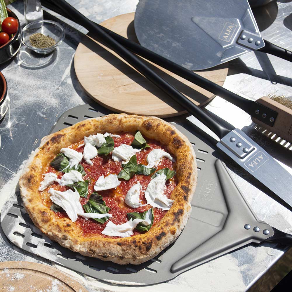 Black-handled pizza peel and turner set on a prep surface with topped pizza