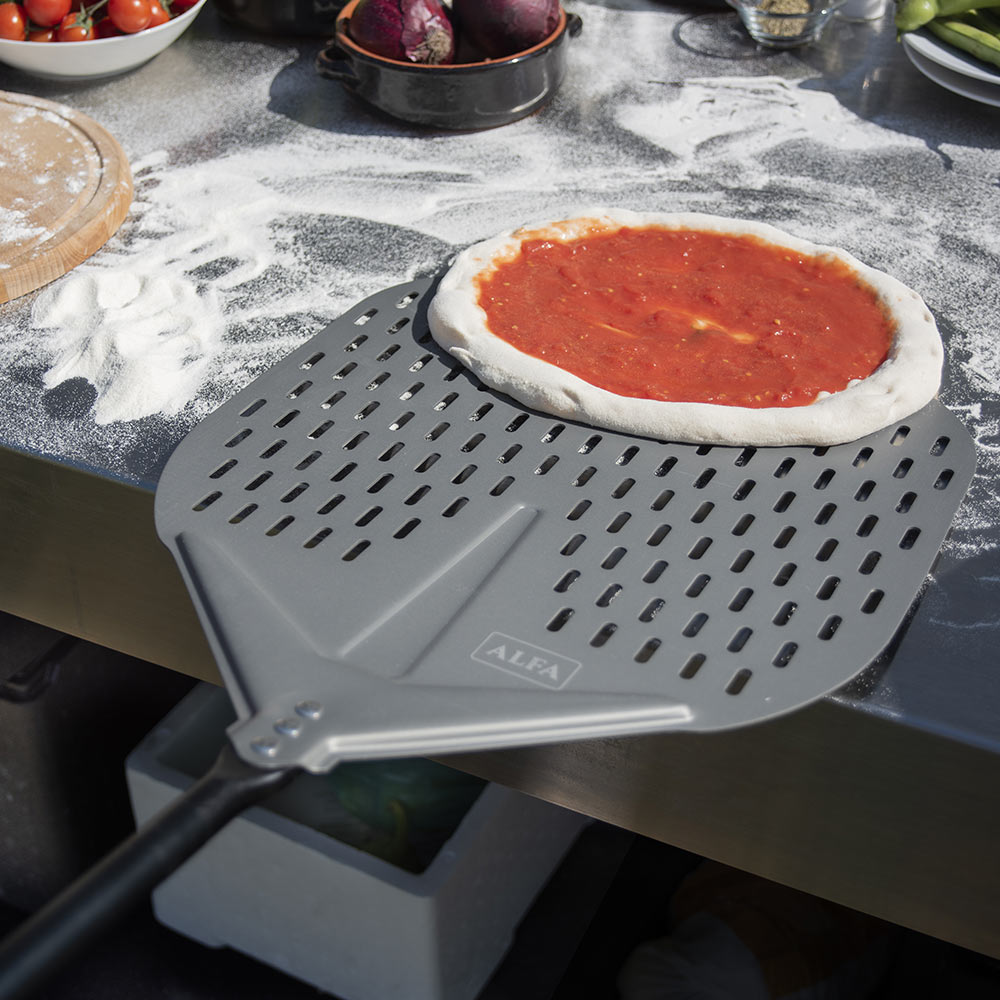 Gray perforated pizza peel holding pizza dough with red sauce