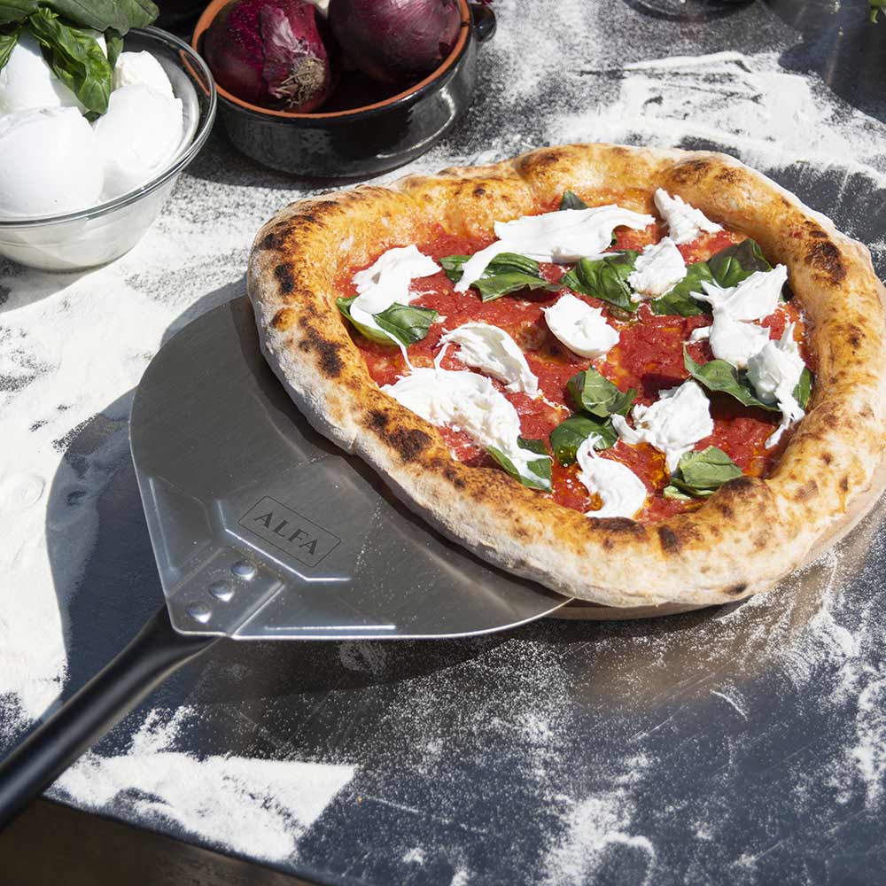 Black-handled metal pizza peel holding topped pizza with greens and cheese