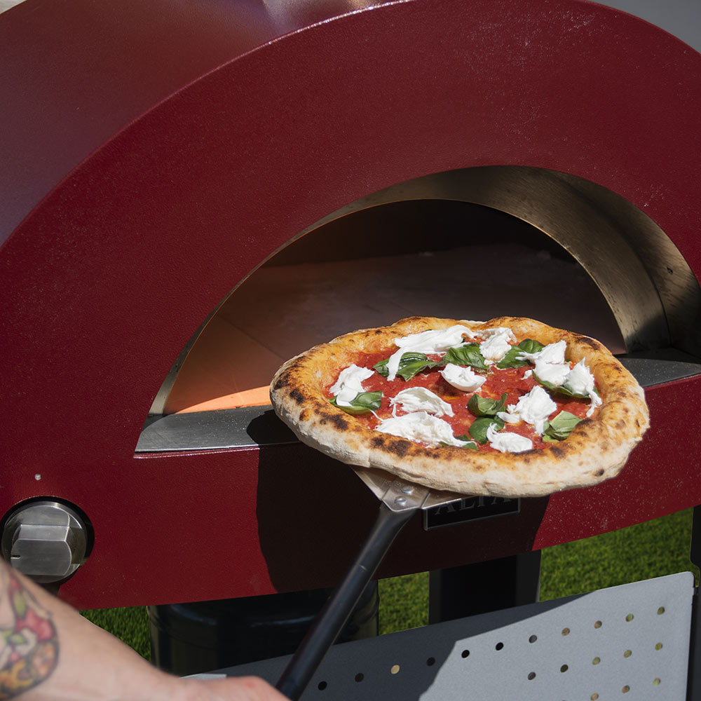 Black-handled metal pizza peel lifting topped pizza from a cook oven
