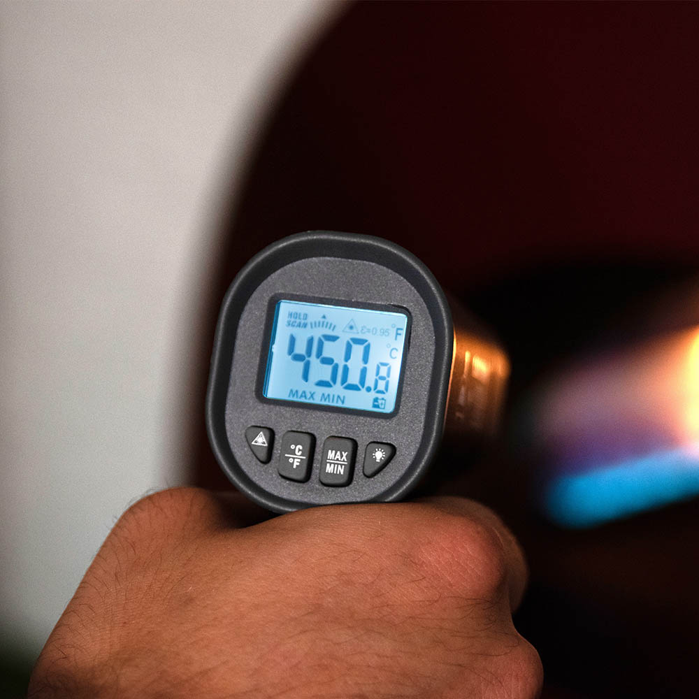 Laser thermometer held in hand, showing LCD temperature reading