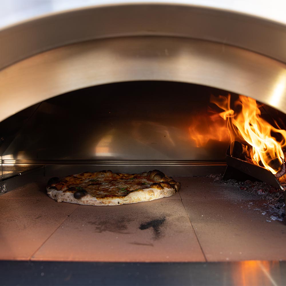 Pizza oven cooking chamber with flames and a pizza on the stone floor
