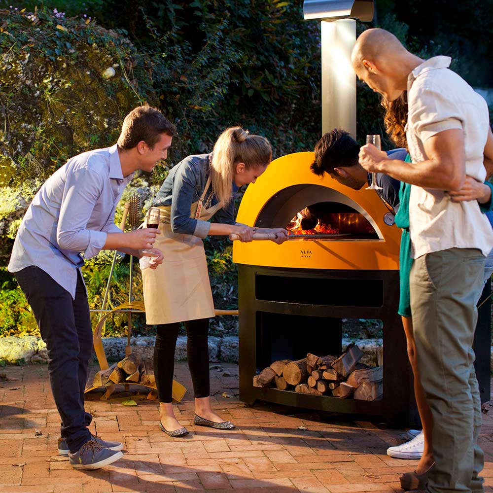Yellow countertop wood-fired pizza oven with open arch while people prepare and serve